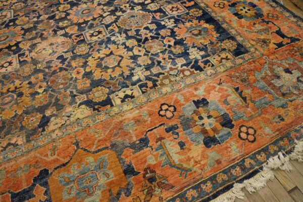 Blue and rust patterned rug with dense floral motifs and fringes lying on light wood planks.