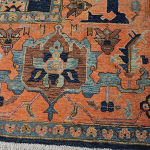 Orange-rust traditional rug detail with navy and light blue designs, a floral border, and white fringe.