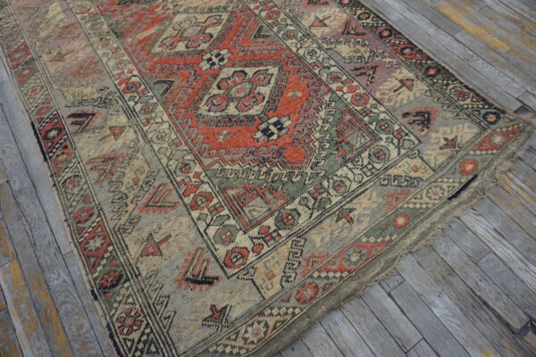 Low-pile geometric rug in faded red, gray, and beige on weathered gray wood plank flooring.