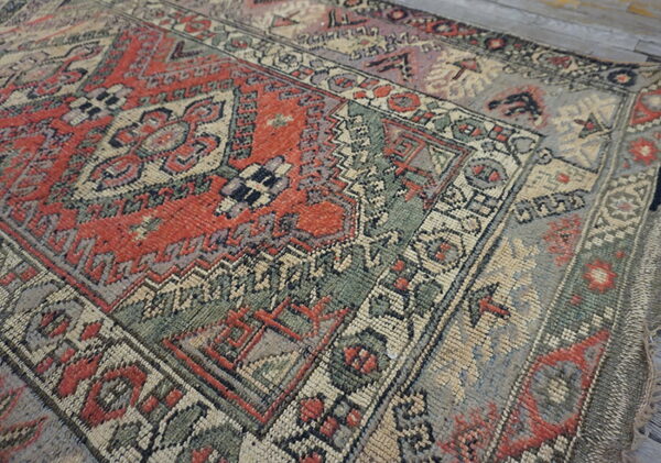 Low-pile geometric rug in distressed red, green, and beige, displayed on light gray wood flooring.