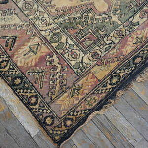 Muted geometric rug in pink, green, and gold on distressed gray wood plank flooring.