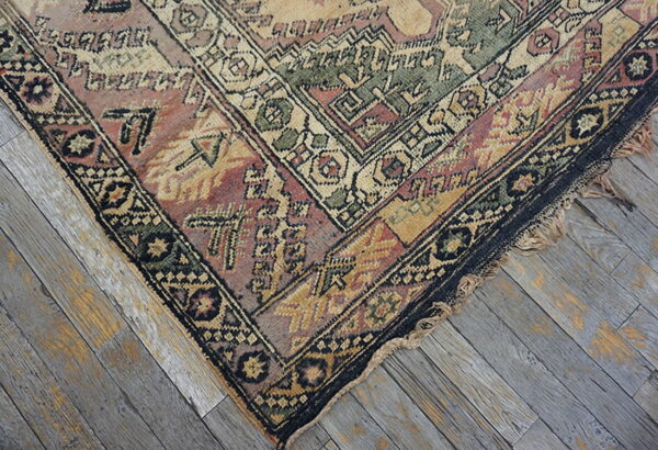Muted geometric rug in pink, green, and gold on distressed gray wood plank flooring.