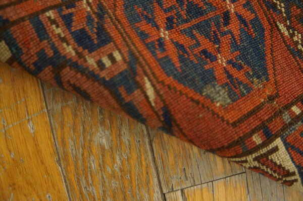 Close-up of a rust, blue, and tan geometric rug edge lying on distressed light wood floors.