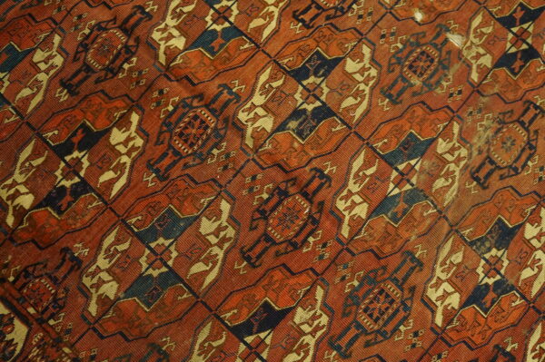 Worn low-pile rug featuring a dense repeating lattice design in rust orange, navy, and gold colors.