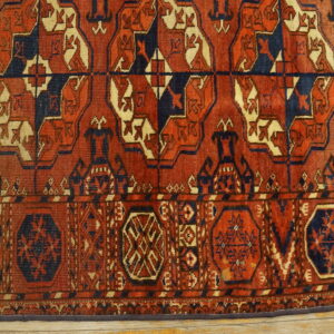 Deep reddish-brown rug with geometric tribal patterns in navy blue and cream over light wood flooring.