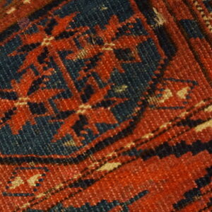 Geometric pattern detail on a low-pile rug featuring colors of deep rust, navy blue, and beige.