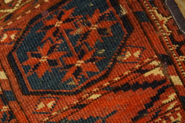 Geometric pattern detail on a low-pile rug featuring colors of deep rust, navy blue, and beige.