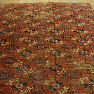Distressed terracotta and navy geometric rug with repeating patterns rests on wide plank wooden flooring.