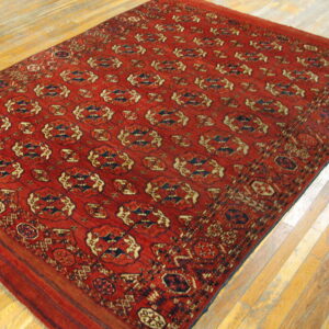 Geometric red area rug with repeating blue and cream patterns displayed on light wooden plank flooring.