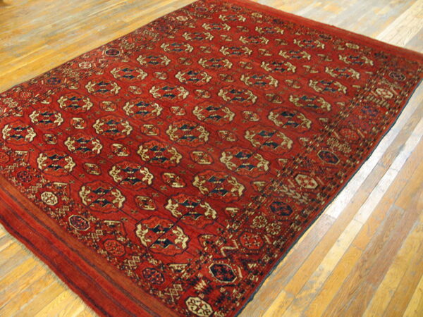 Geometric red area rug with repeating blue and cream patterns displayed on light wooden plank flooring.
