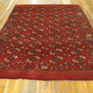 Rectangular rug in deep red with repeating navy and beige geometric medallions on wood flooring.