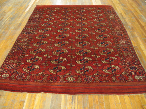 Rectangular rug in deep red with repeating navy and beige geometric medallions on wood flooring.