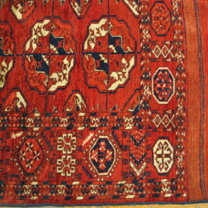 Red rug with geometric patterns in navy and cream, showing main field, border, and fringed end.