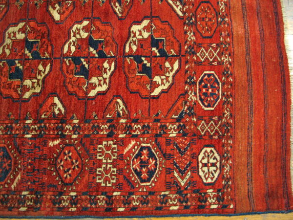 Red rug with geometric patterns in navy and cream, showing main field, border, and fringed end.