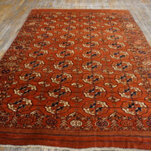 Rust-colored rug featuring navy and cream repeating geometric gul motifs on a distressed wood floor.