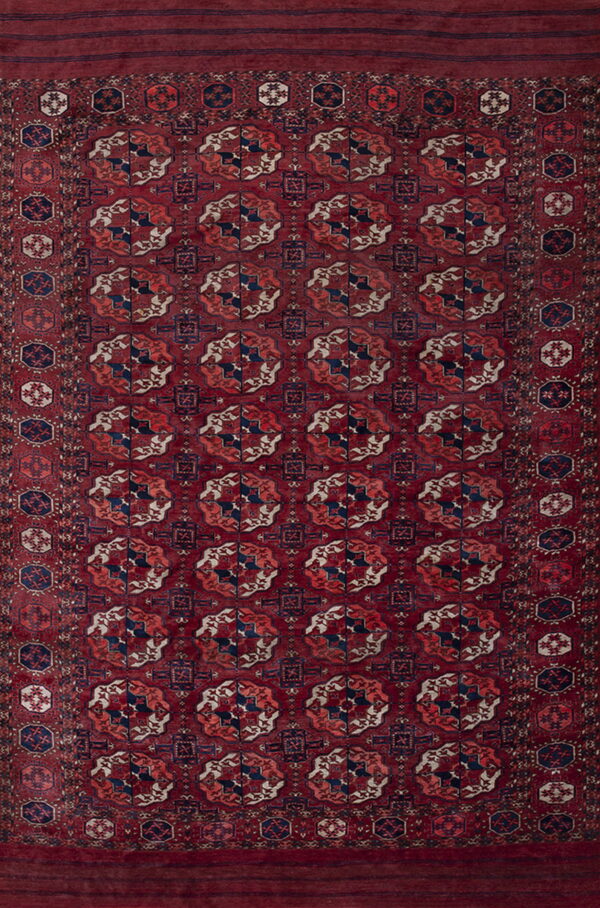 A burgundy low-pile rug featuring repeating navy, rust, and cream geometric tribal motifs.