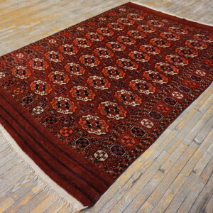 Red rug with repeating octagonal orange and navy patterns sits on weathered gray wood floor.