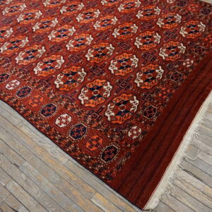 Red geometric medallion rug with navy and orange accents lies on rustic gray wood flooring.