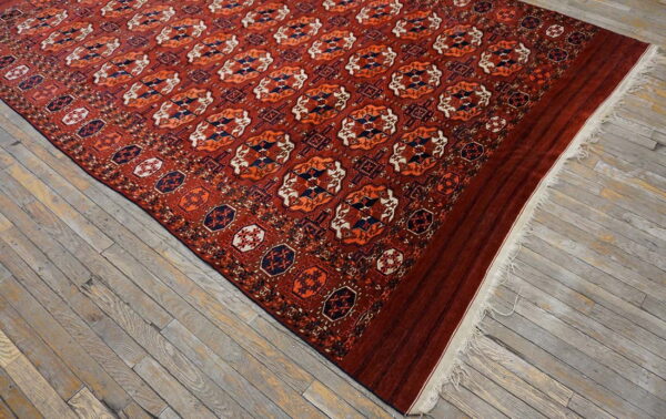 Red geometric medallion rug with navy and orange accents lies on rustic gray wood flooring.