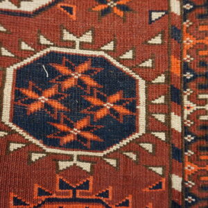 Geometric rug detail showing a navy octagon with orange stars on a rich maroon field.