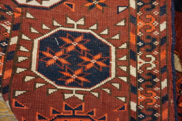 Geometric rug detail showing a navy octagon with orange stars on a rich maroon field.