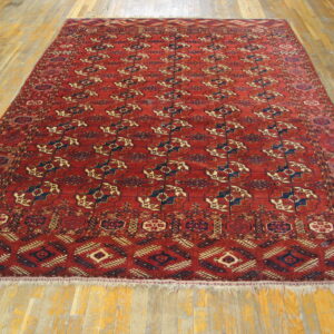 Red, low-pile area rug with traditional blue and tan geometric patterns on light hardwood floors.