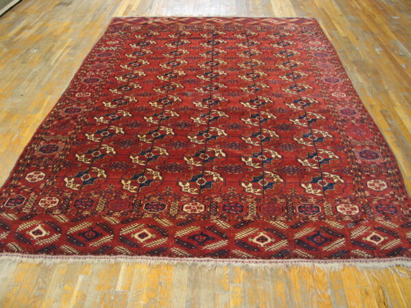 Red, low-pile area rug with traditional blue and tan geometric patterns on light hardwood floors.