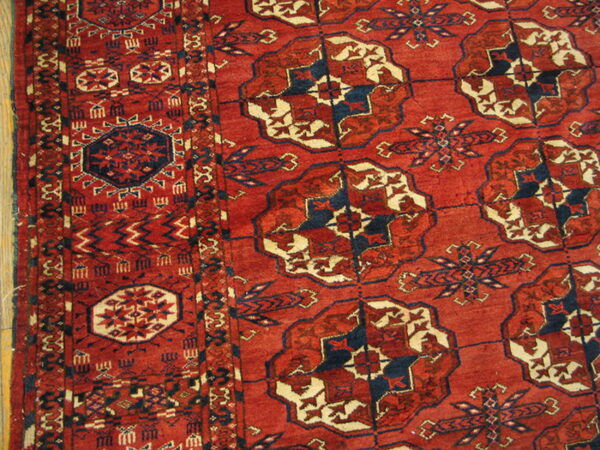 Red rug with geometric blue and cream medallions and a detailed border on wood flooring.