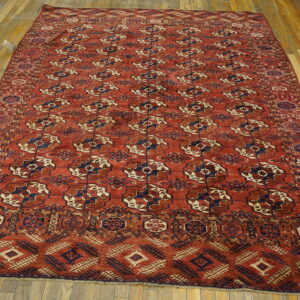 Red rug with repeating navy and tan medallions and complex borders laid on light wooden plank flooring.