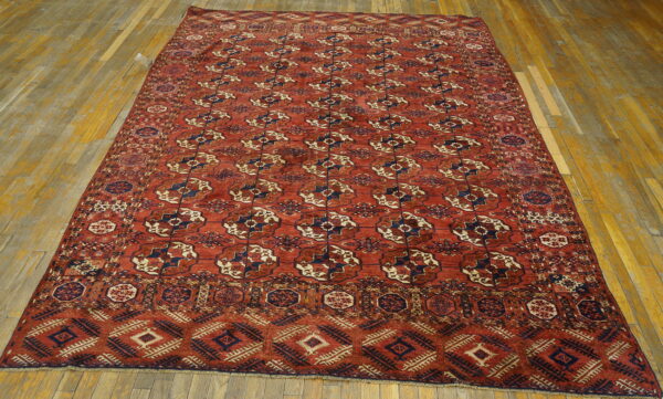 Red rug with repeating navy and tan medallions and complex borders laid on light wooden plank flooring.