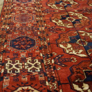 Red, navy, and cream geometric rug with patterned borders sits angled on light wood flooring.