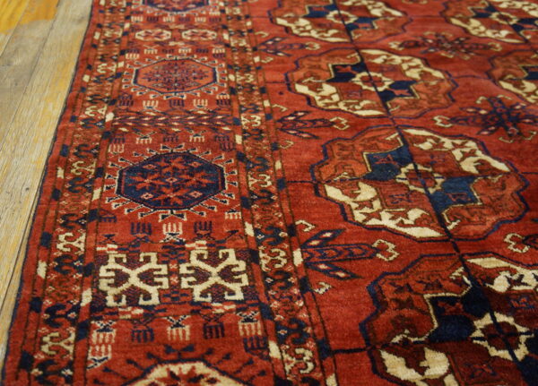 Red, navy, and cream geometric rug with patterned borders sits angled on light wood flooring.