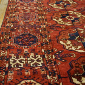 Close-up of a red, navy, and cream geometric rug border resting on distressed light wood floors.