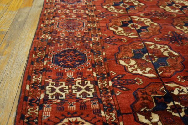 Close-up of a red, navy, and cream geometric rug border resting on distressed light wood floors.