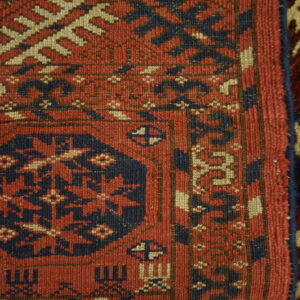 Detail of a red and navy geometric low-pile rug adjacent to a deeper red and tan patterned rug.