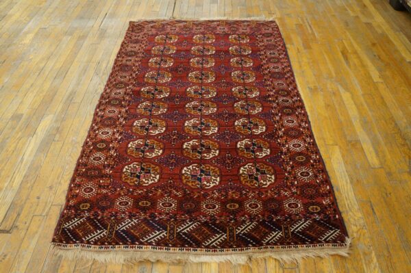 Red rug with repeating geometric guls in blue, gold, and white rests on light wood floors.