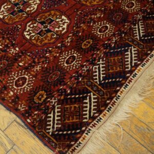Geometric red and dark blue rug with cream fringe on exposed, light-toned wood flooring.