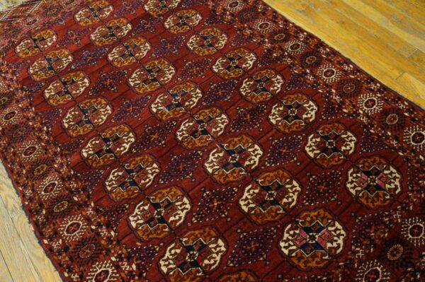 Burgundy rug with repeating geometric medallions and detailed borders laid over light hardwood planks.