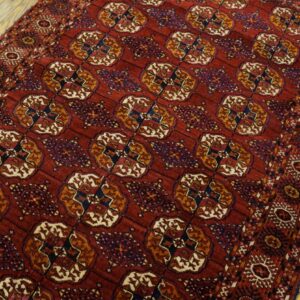 Red patterned rug featuring repeating geometric medallions in gold, blue, and cream on light wood planks.