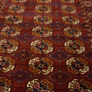Red area rug with detailed gold, navy, and cream repeating geometric patterns on wooden flooring.