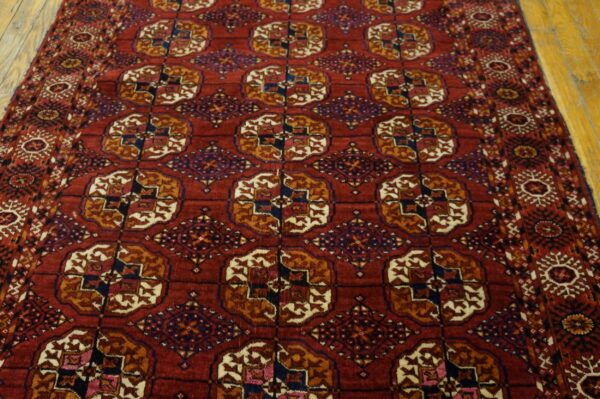 Red area rug with detailed gold, navy, and cream repeating geometric patterns on wooden flooring.