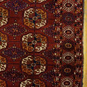 Close-up of a deep red rug featuring octagonal medallions and geometric borders lying on worn yellow wood floors.