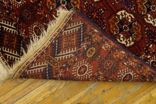 Red geometric rug pile and woven backing are visible where the corner is folded on light wood planks.