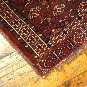A deep red geometric rug with cream and blue patterns rests on bright, distressed hardwood flooring.