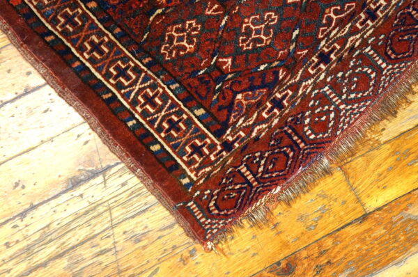 A deep red geometric rug with cream and blue patterns rests on bright, distressed hardwood flooring.