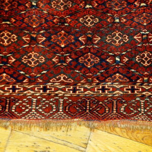 Red and navy geometric patterned rug fringe laying on light golden hardwood planks.