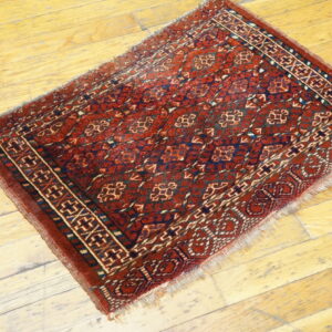 Small, traditional red and navy rug with geometric patterns is placed on light wooden flooring.