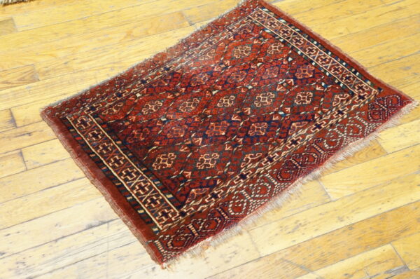 Small, traditional red and navy rug with geometric patterns is placed on light wooden flooring.