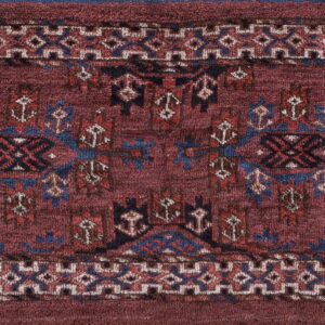Low-pile rug with a deep red field and geometric tribal patterns in blue, tan, and black.