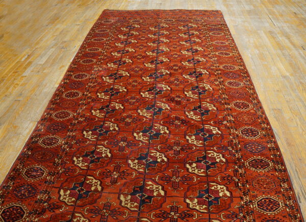 Long reddish-orange runner rug with geometric medallions in navy and cream on light wood flooring.